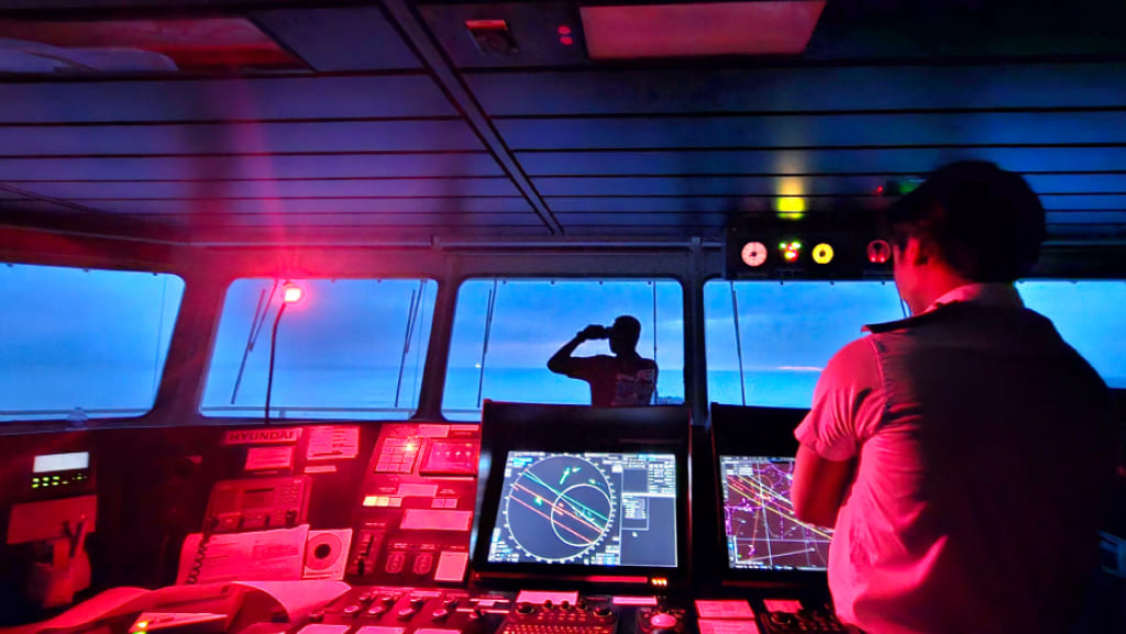 Chief Officer Joebert Canja navigating a vessel at night inside a ship’s bridge lit with red tactical lighting.
