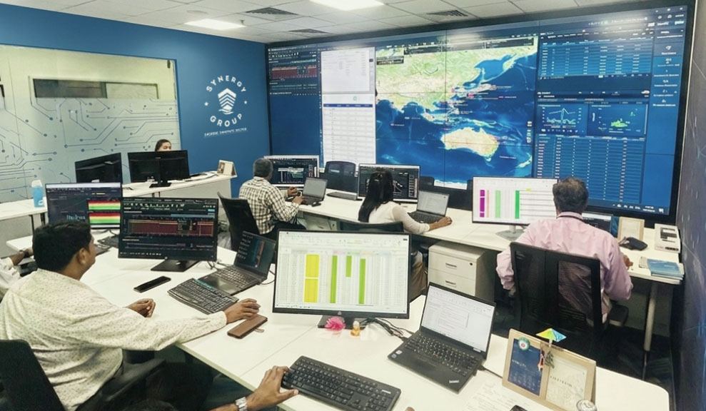 Maritime operations team tracking fleet data on individual monitors and a large video wall display inside the Synergy Group control center.