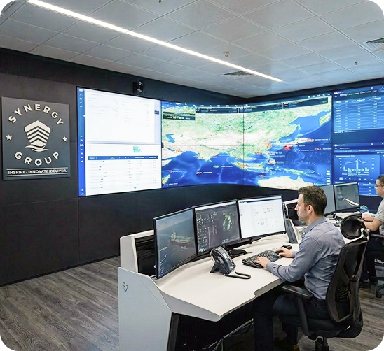 Operators working inside the modern Synergy Group marine operations center with large wall displays tracking global vessel positions.