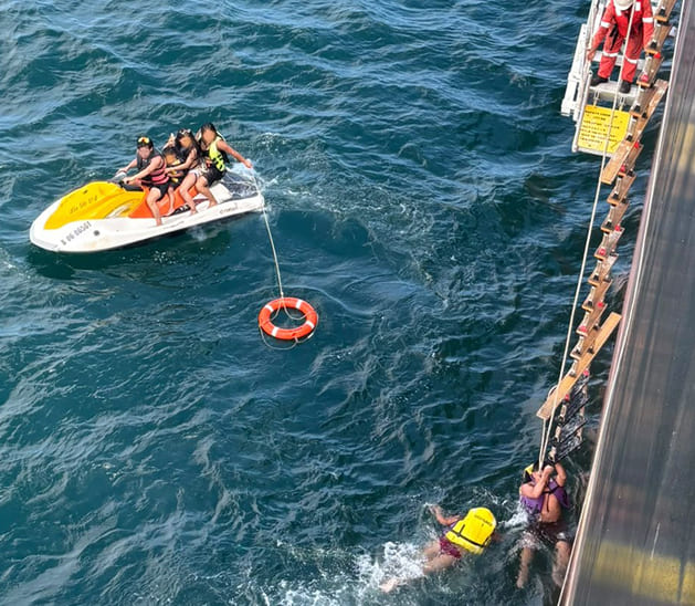 Maritime rescue operations showing a jet ski and individuals in life jackets alongside a ship's pilot ladder.