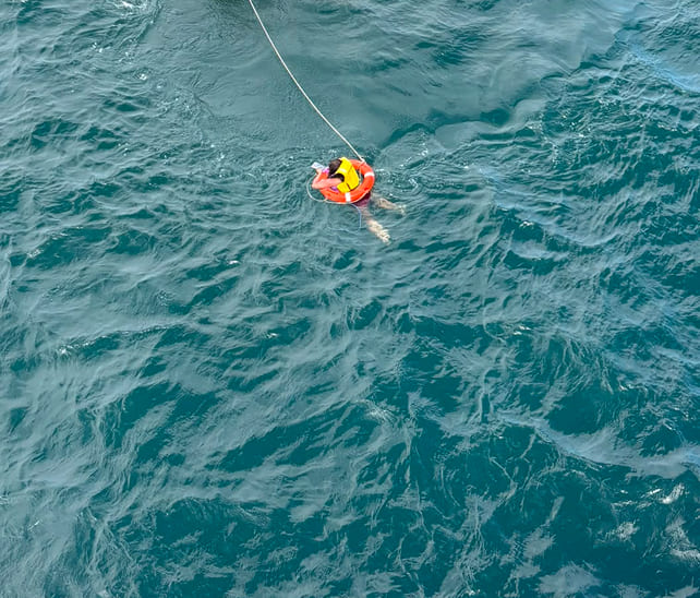 Overhead view of a person in a lifebuoy being pulled through the ocean during a maritime rescue operation.